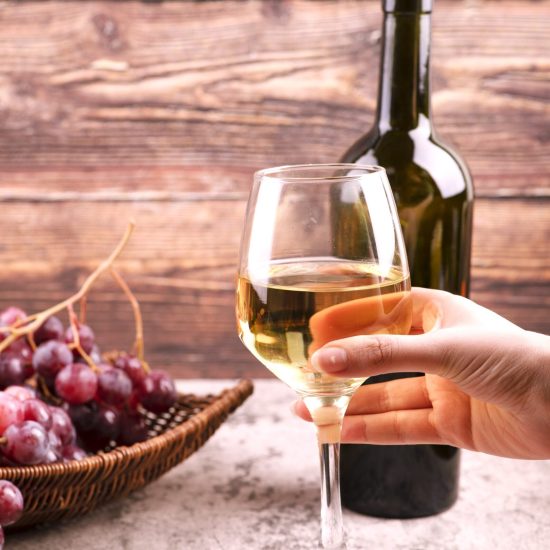 Female hand holding glass of white wine on marble table